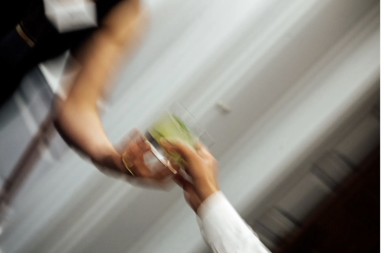 blury picture of a clear drink with lime slices being passed from one hand to another