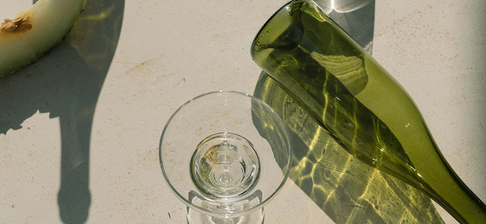 Green glass bottle and martini glass with a slice of green fruit in the upper left corner