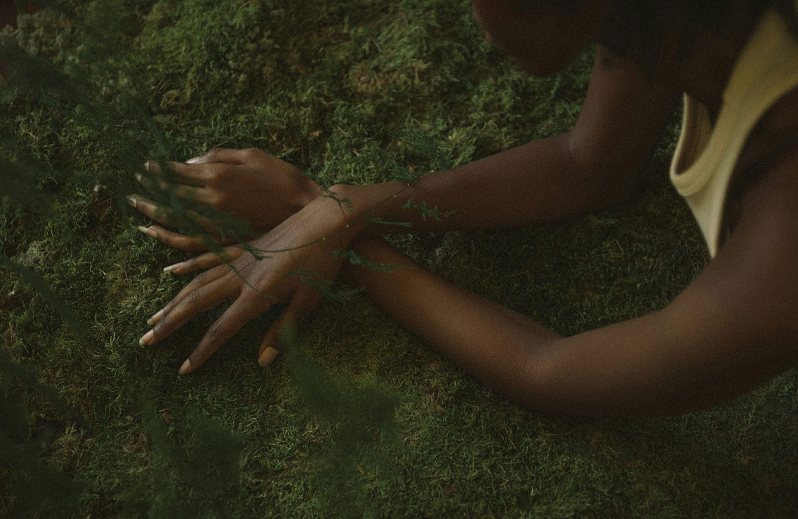 a woman lying on dark grass wearing a yellow shirt