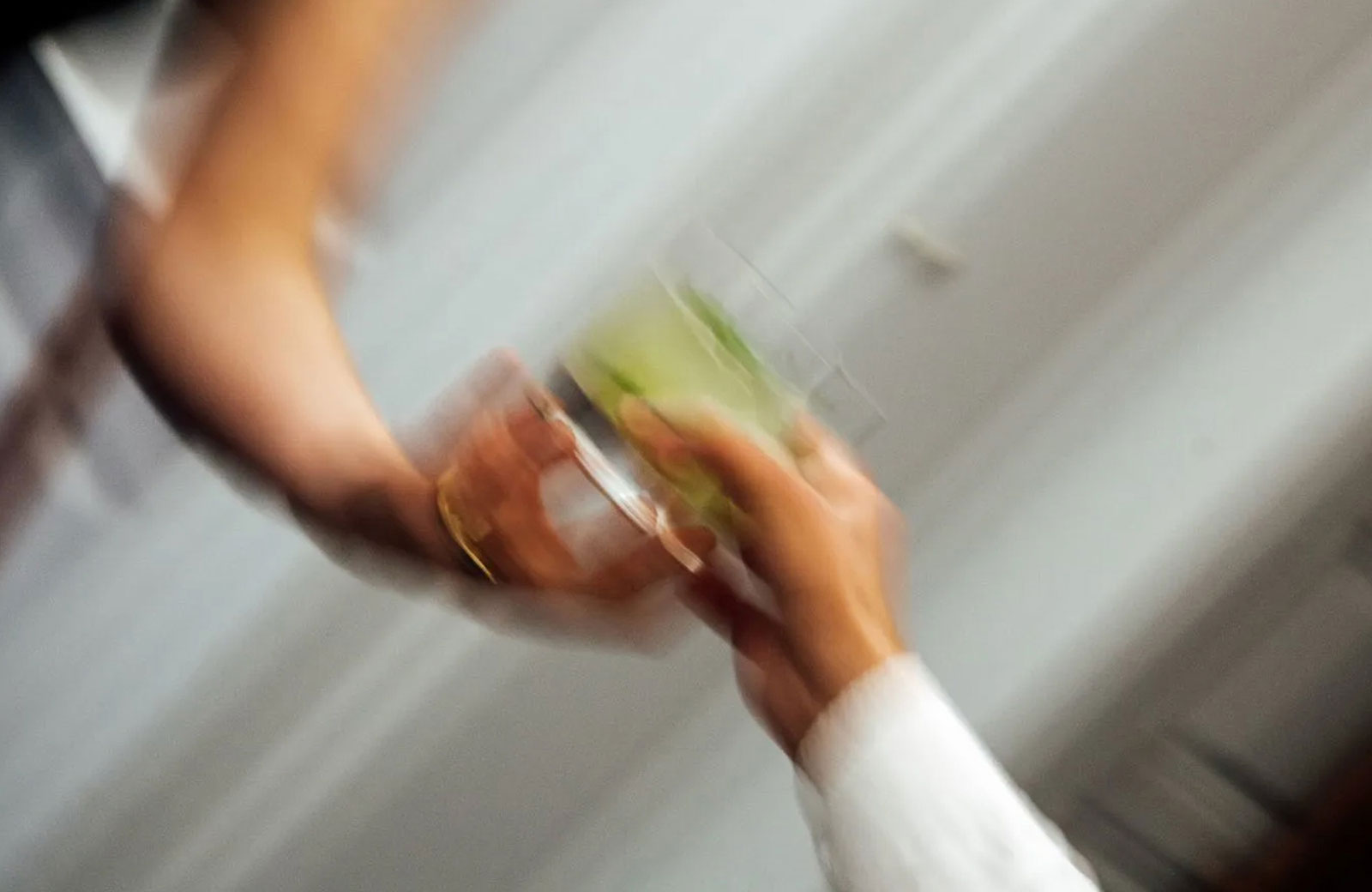 Close-up photo of a man passing a green cocktail to a woman wearing a gold bracelet